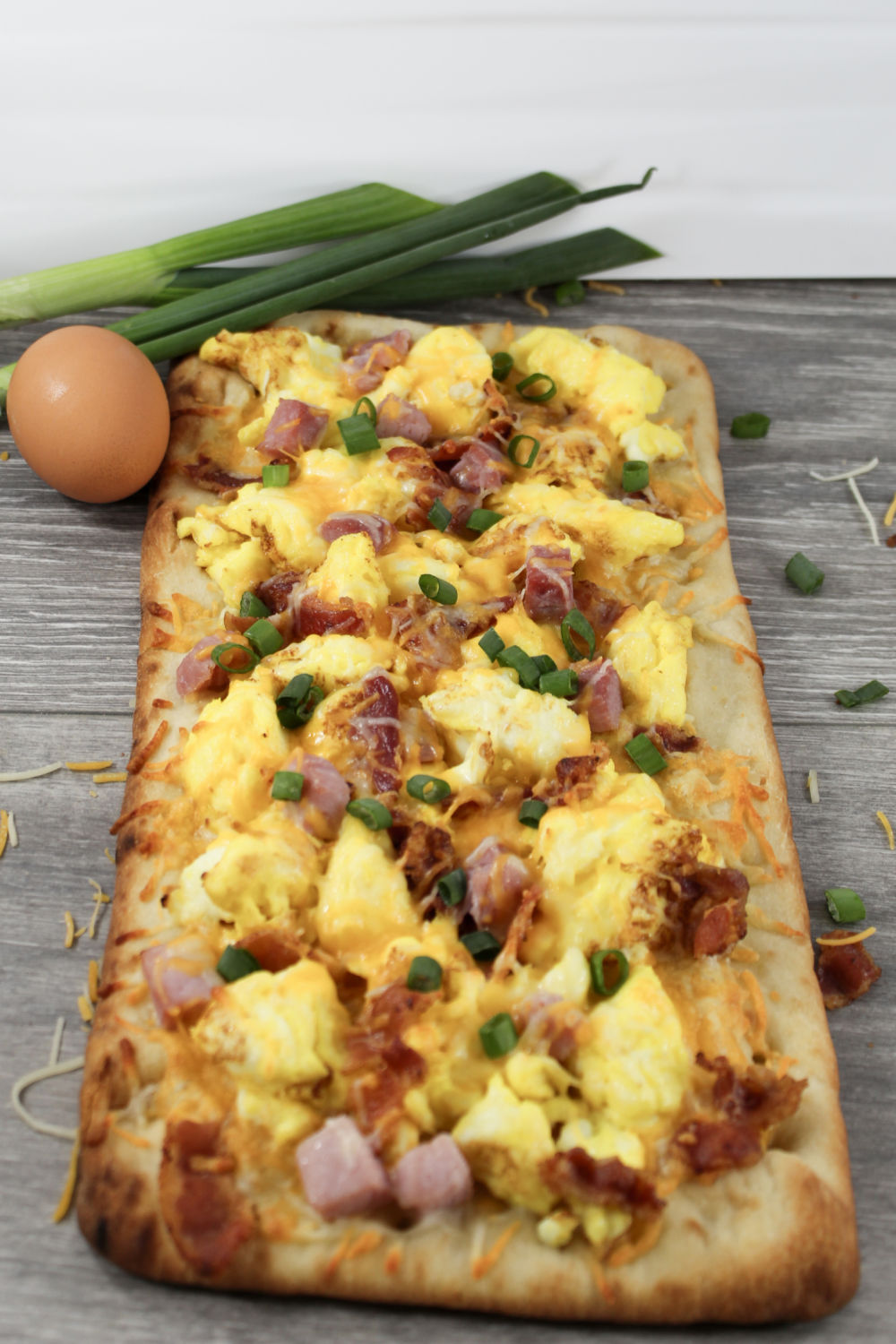 vertical image of flatbread breakfast pizza with eggs and bacon