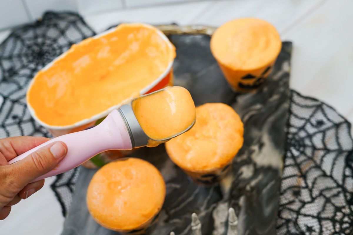 scooping orange sherbet in plastic cups