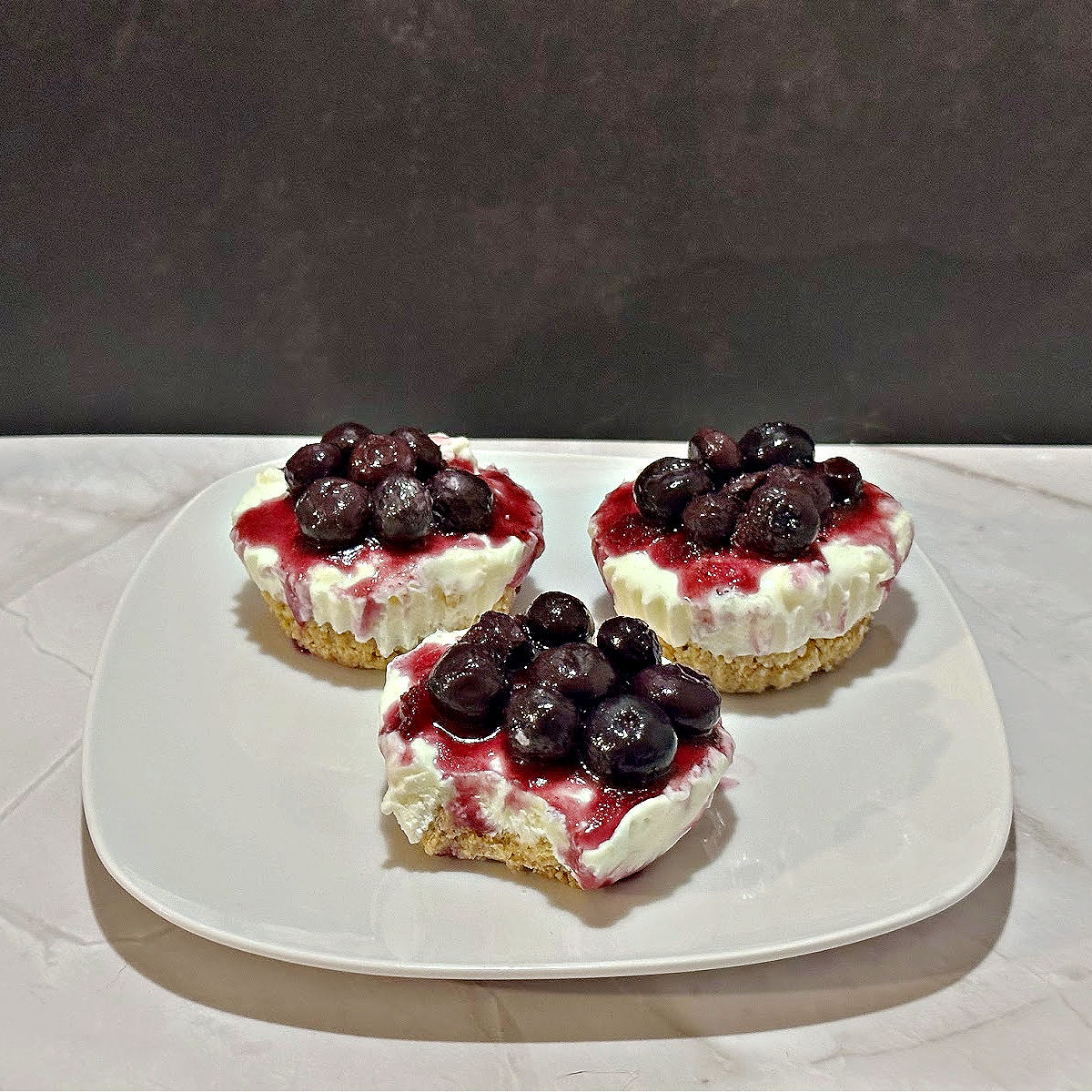 no bake cheesecake bites on white plate with blueberry sauce